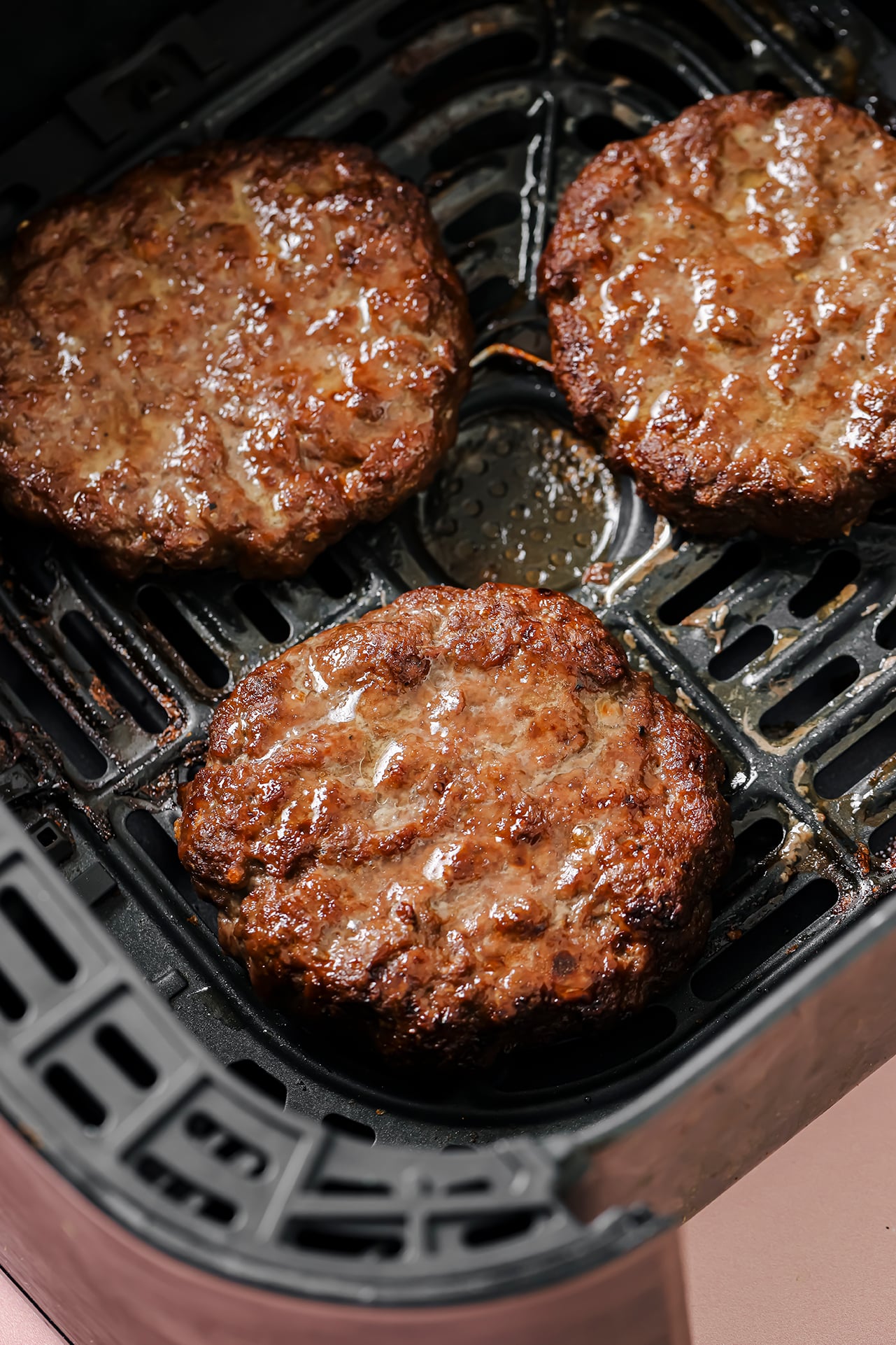 Three air fryer burgers fully cooked in the air fryer basket.