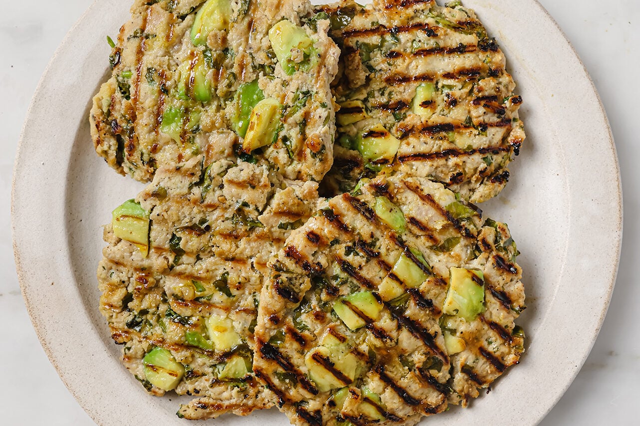 Grilled avocado chicken burgers on a white plate.