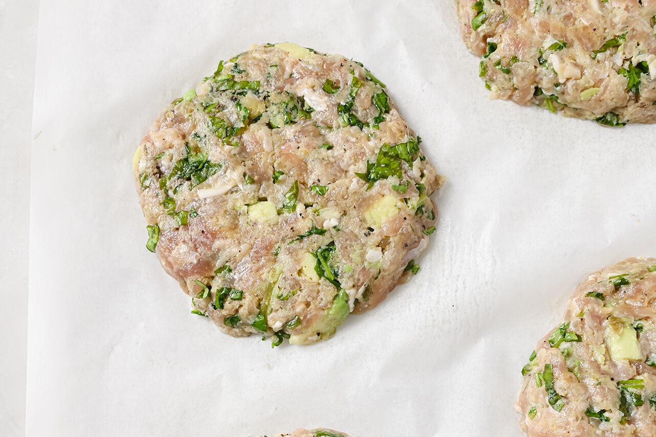Avocado chicken burgers uncooked on a piece of parchment paper. 