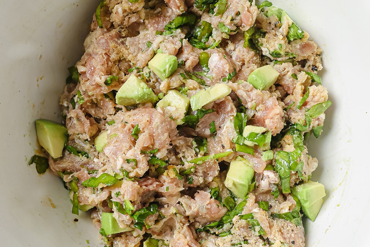 Ground chicken, spinach and herbs mixed in a bowl with diced avocado. 