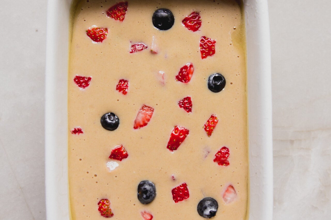 The batter for berry protein breakfast cake added to the ceramic baking dish with extra berries on top before baking.