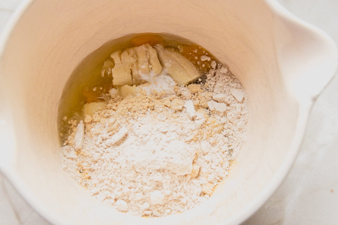 A white ceramic bowl with banana, flour, and protein powder added to the bowl before blending it.