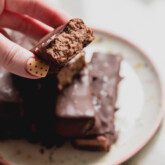 Brownie marshmallow protein bars on a plate with one cut in half and being held.