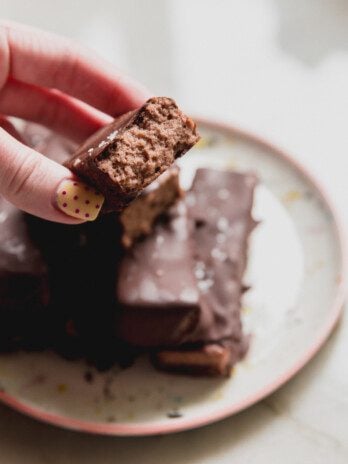 Brownie marshmallow protein bars on a plate with one cut in half and being held.