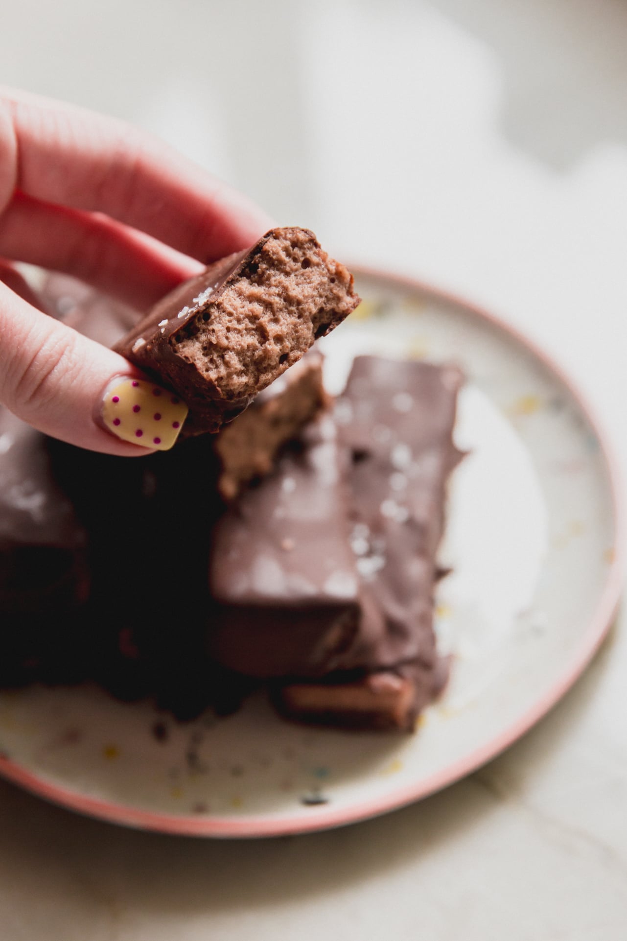 Brownie marshmallow protein bars on a plate with one cut in half and being held.