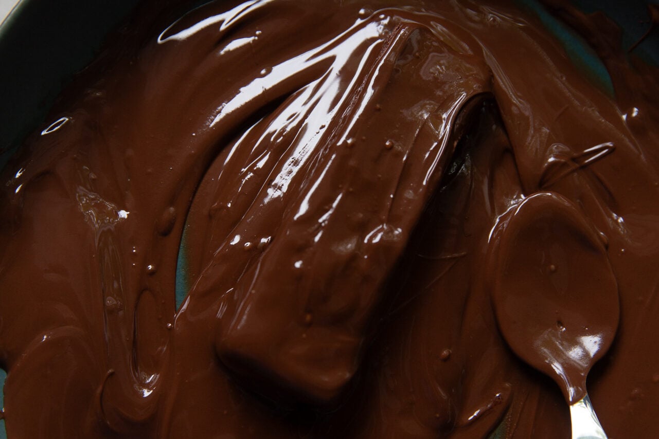 A blue bowl filled with melted chocolate chips and coconut oil that has been mixed with a metal spoon.
