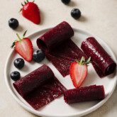 Fruit roll ups on a white plate with fresh berries.