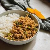Orange ground chicken bowls in a bowl with rice and orange slices in the backround.