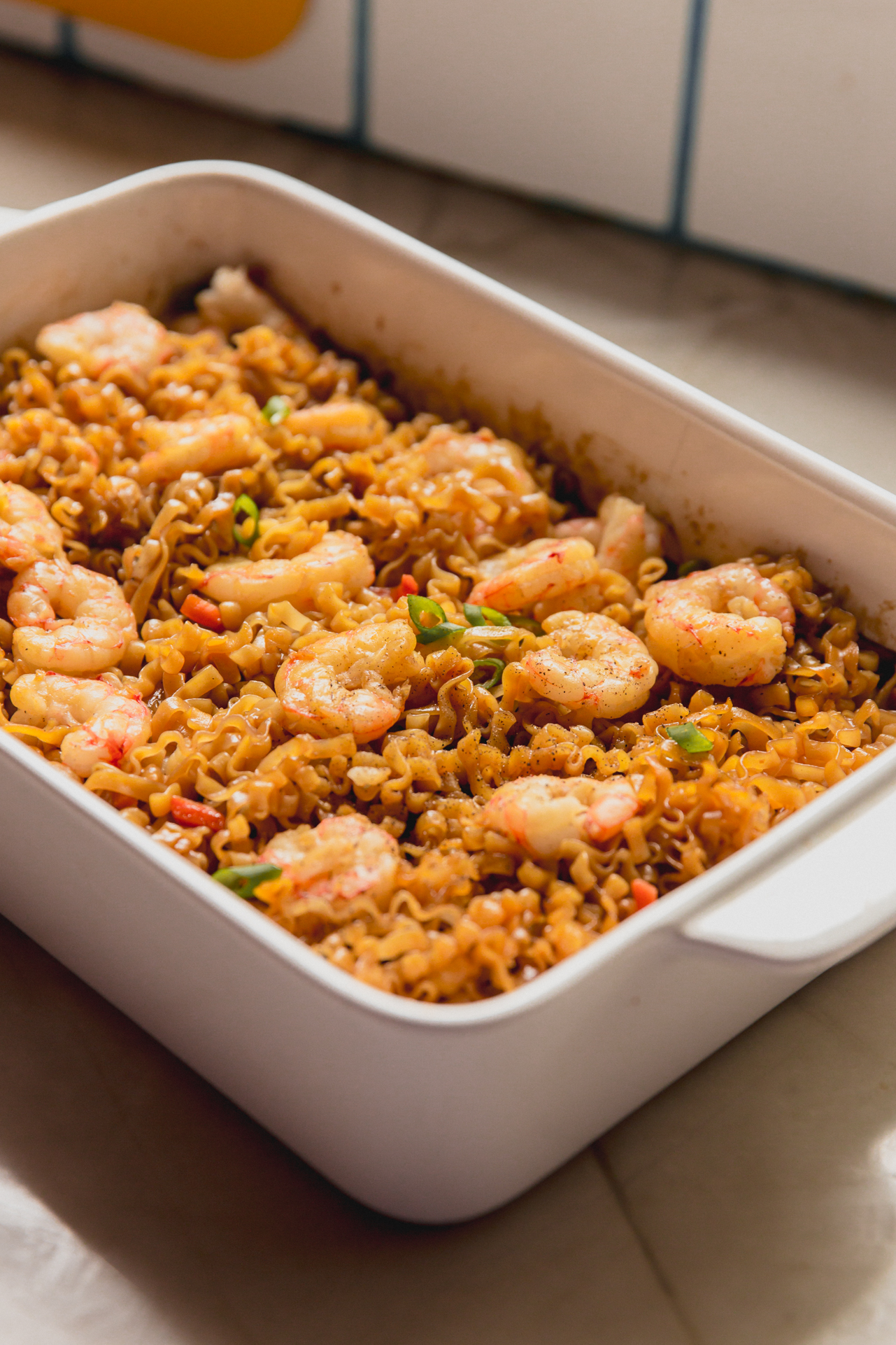 Cooked shrimp and ramen in a large white glass baking dish.