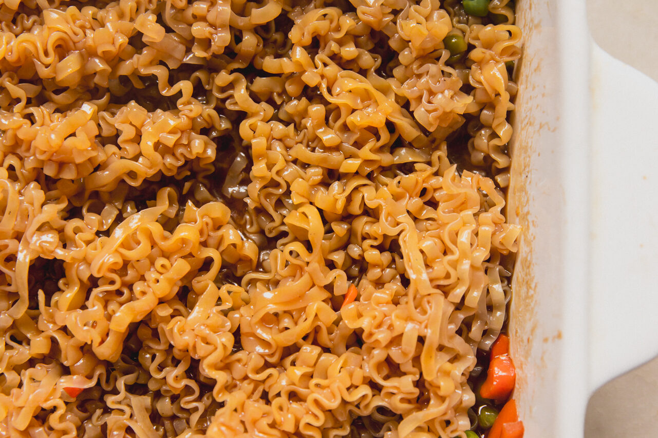 A white casserole dish with mixed vegetable, sauce, and ramen mixed in it.