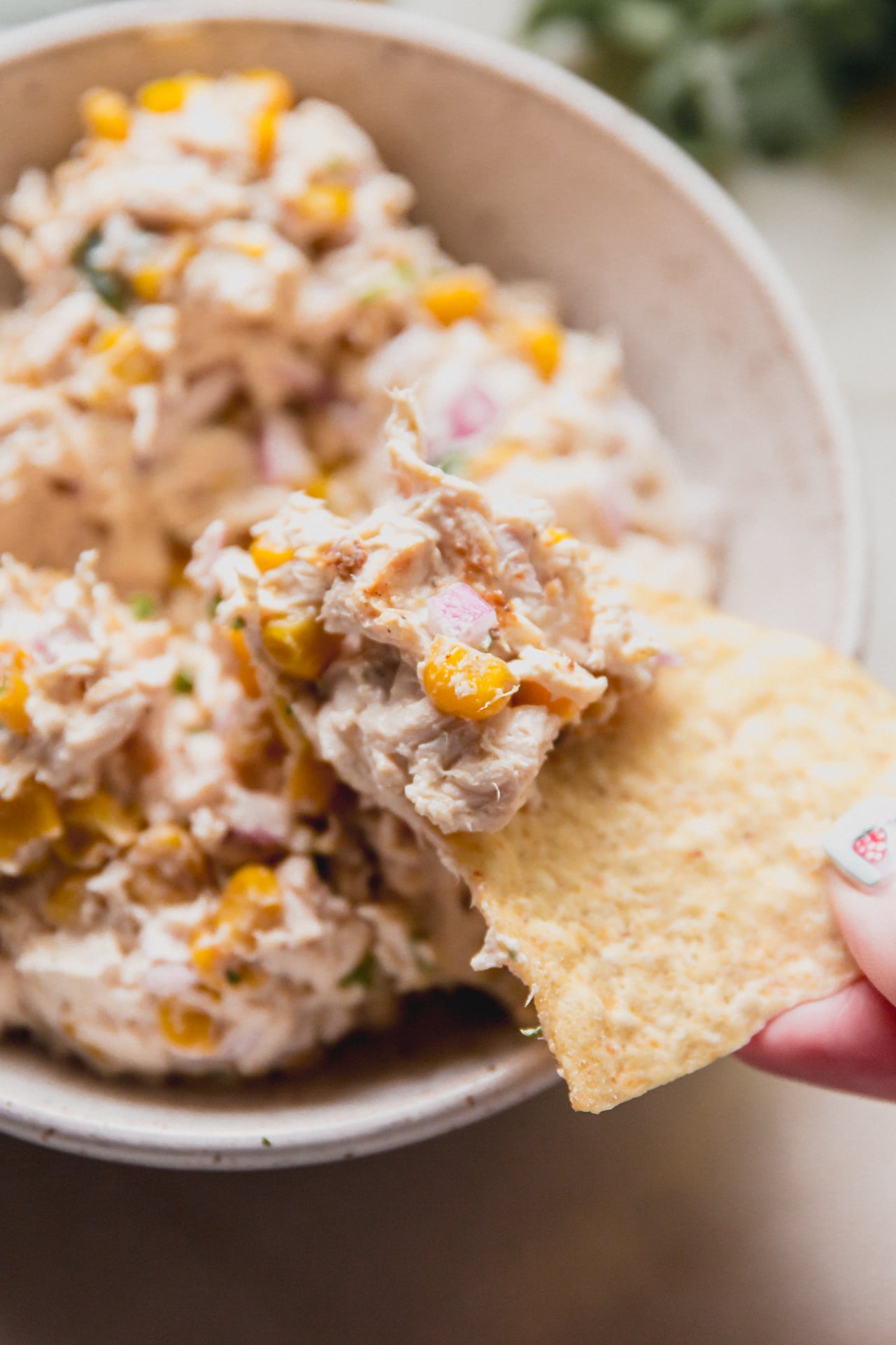 A chip taking a chunk of street corn chicken salad from the bowl.