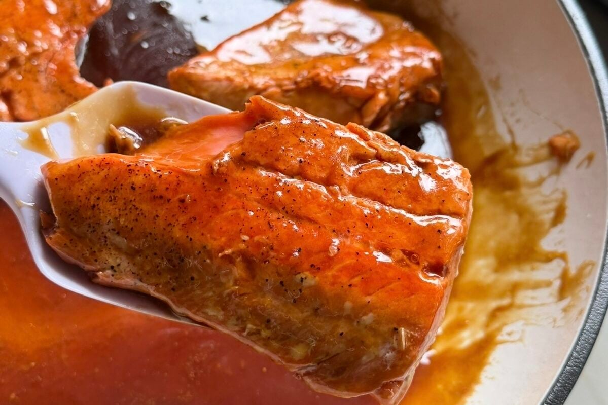 Teriyaki salmon being lifted out of a pan with extra sauce.