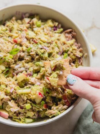 Avocado tuna salad in a bowl with a cracker dipping in.