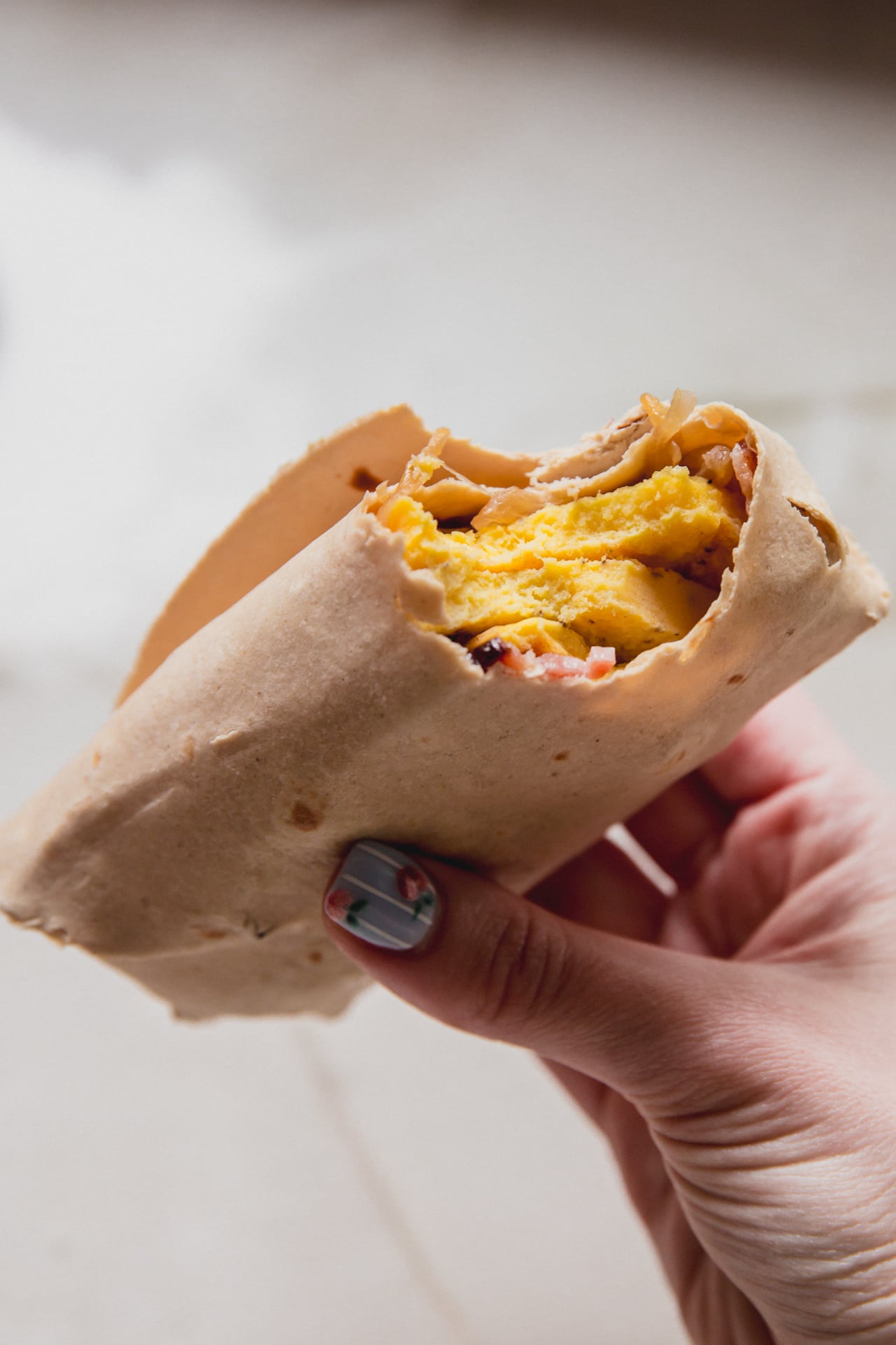 A hand holding a caramelized onion breakfast burrito with a bite taken out of it.