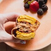 Breakfast burrito cut in half being held on a plate with berries.