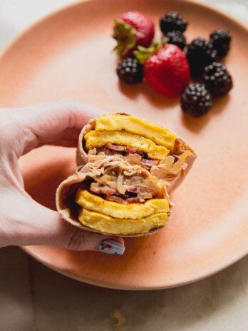 Breakfast burrito cut in half being held on a plate with berries.