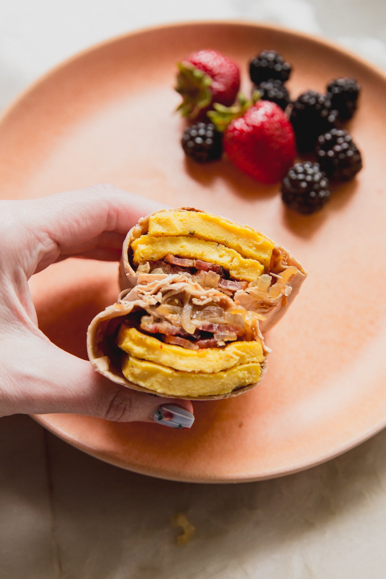 Breakfast burrito cut in half being held on a plate with berries.
