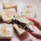 Ice cream cake bite with a cookie and ice cream layer being held with a hand, and a bite taken out.