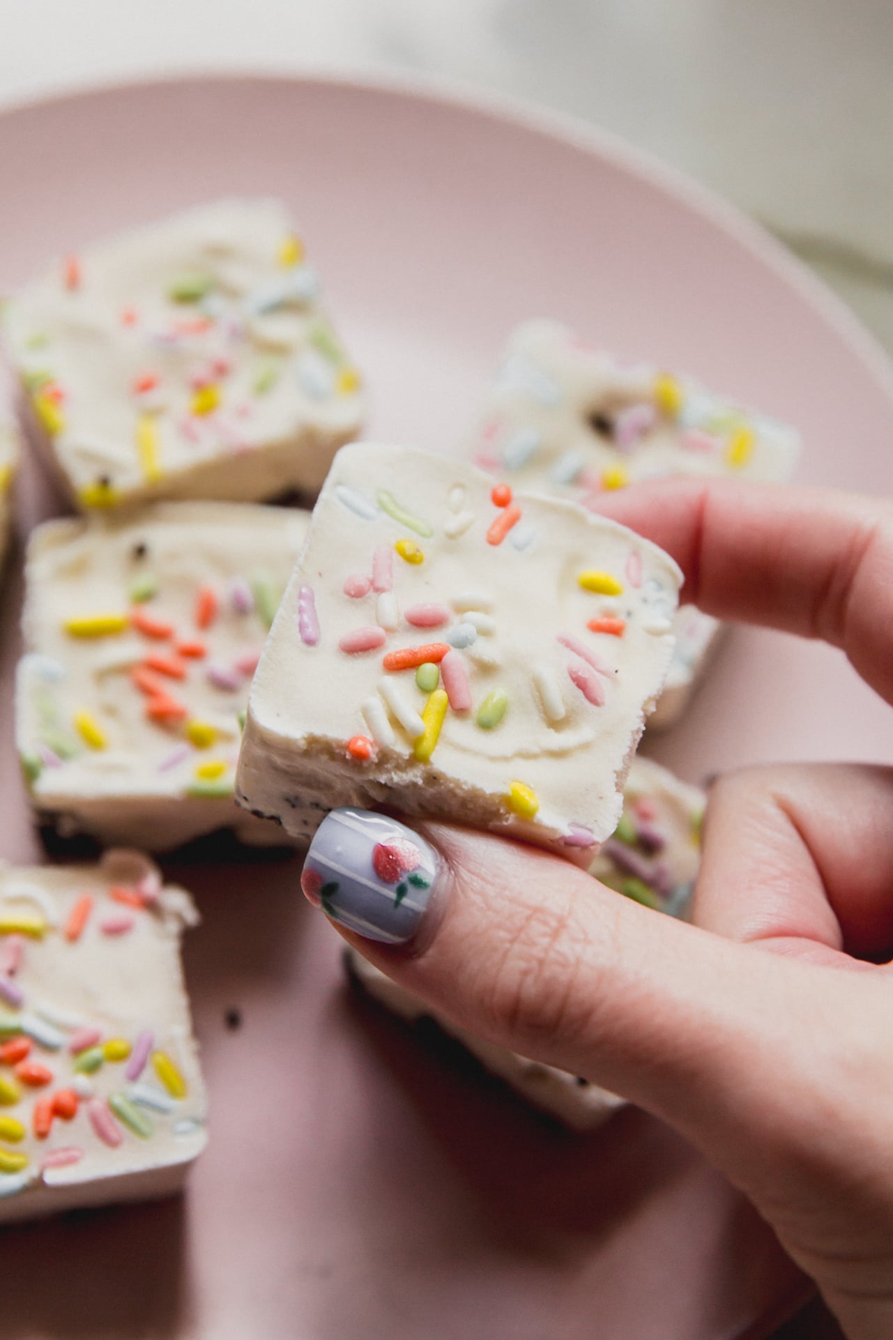 A hand holding a ice cream cake bite above a plate stacked with them.