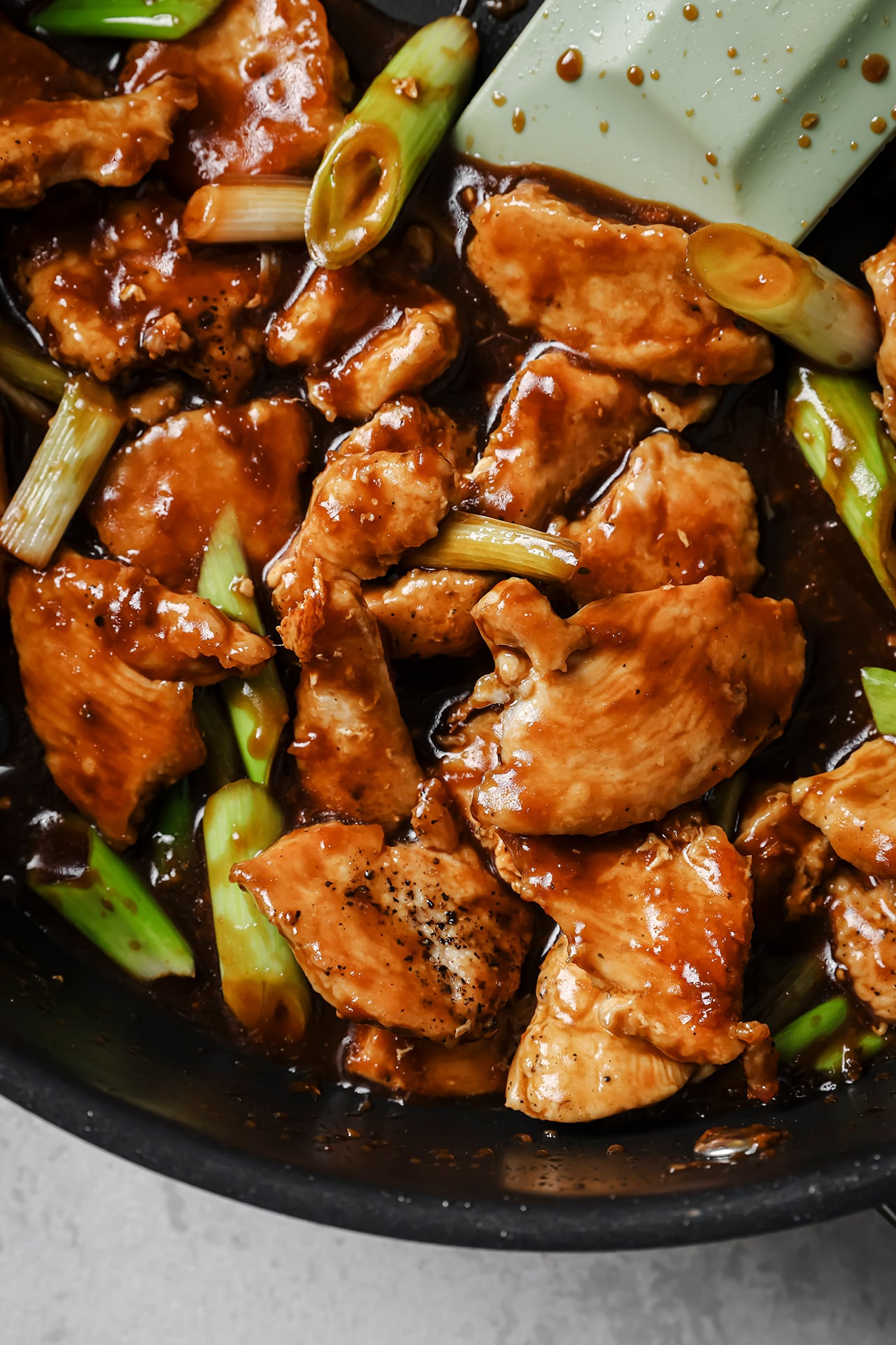 Cooked mongolian chicken and green onions coated in sauce in a pan.