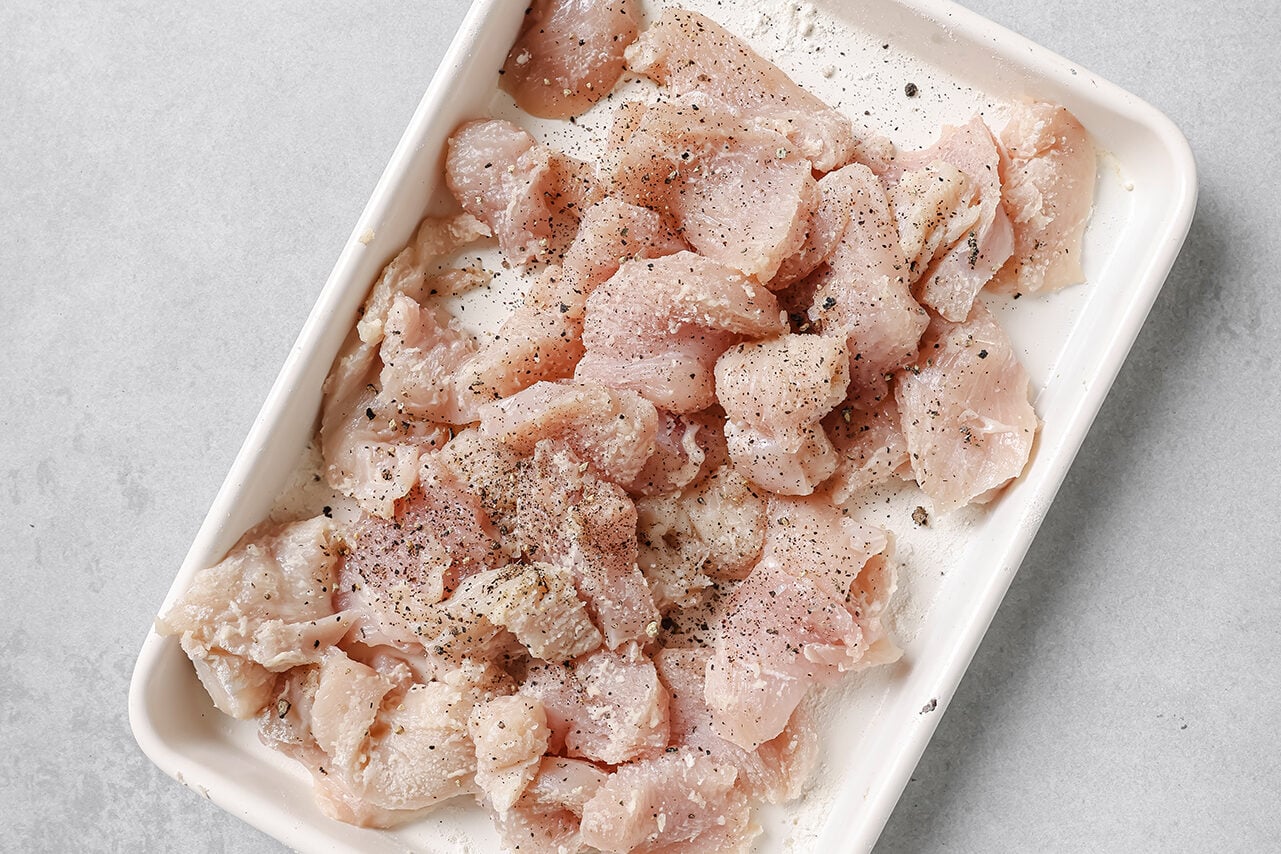 Cubed chicken tossed with arrowroot starch in a pan.