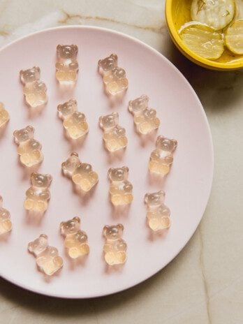 Pickle juice gummy bears on a plate with a bowl of pickles on the side.