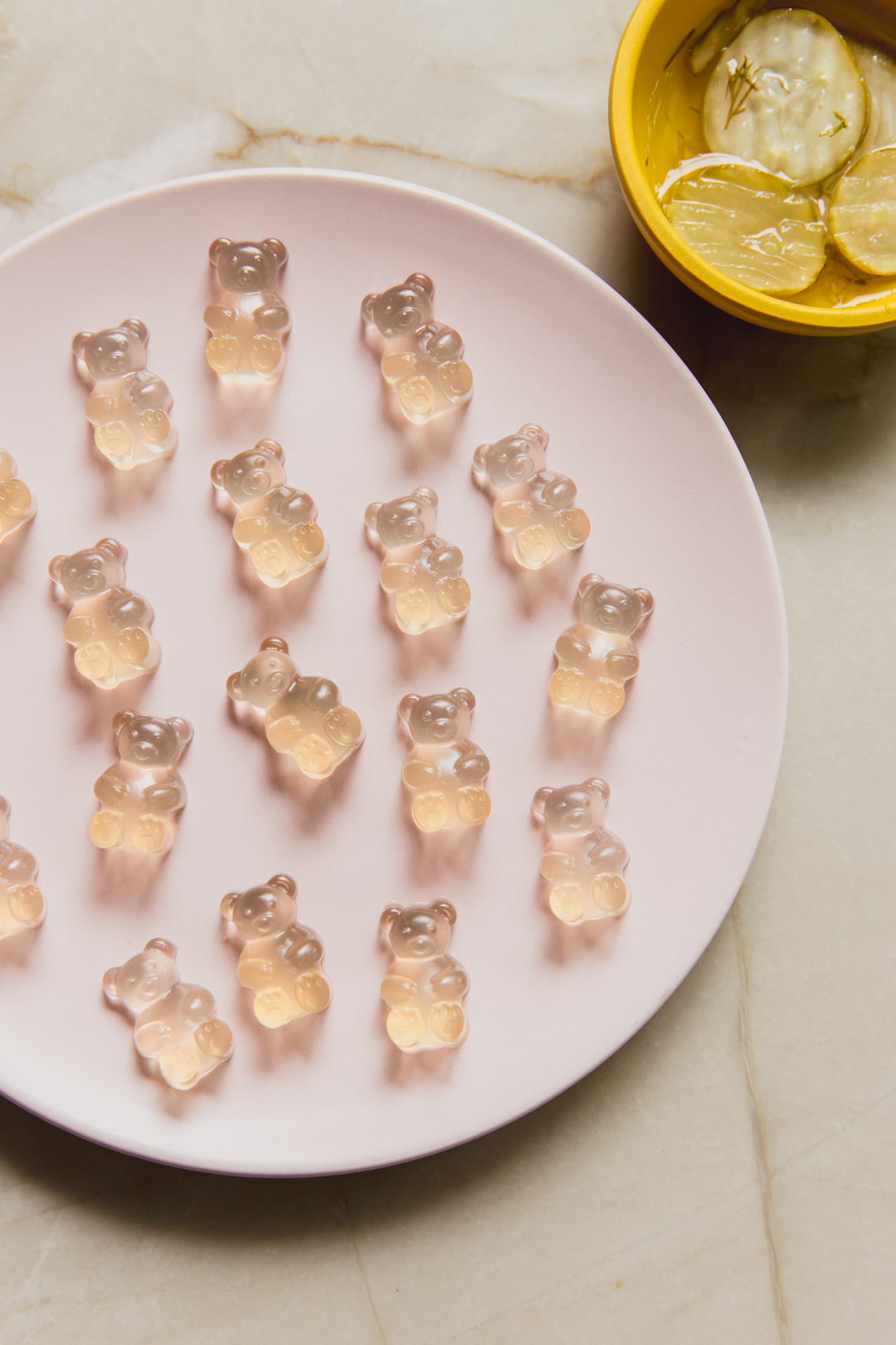Pickle juice gummy bears on a plate with a bowl of pickles on the side.