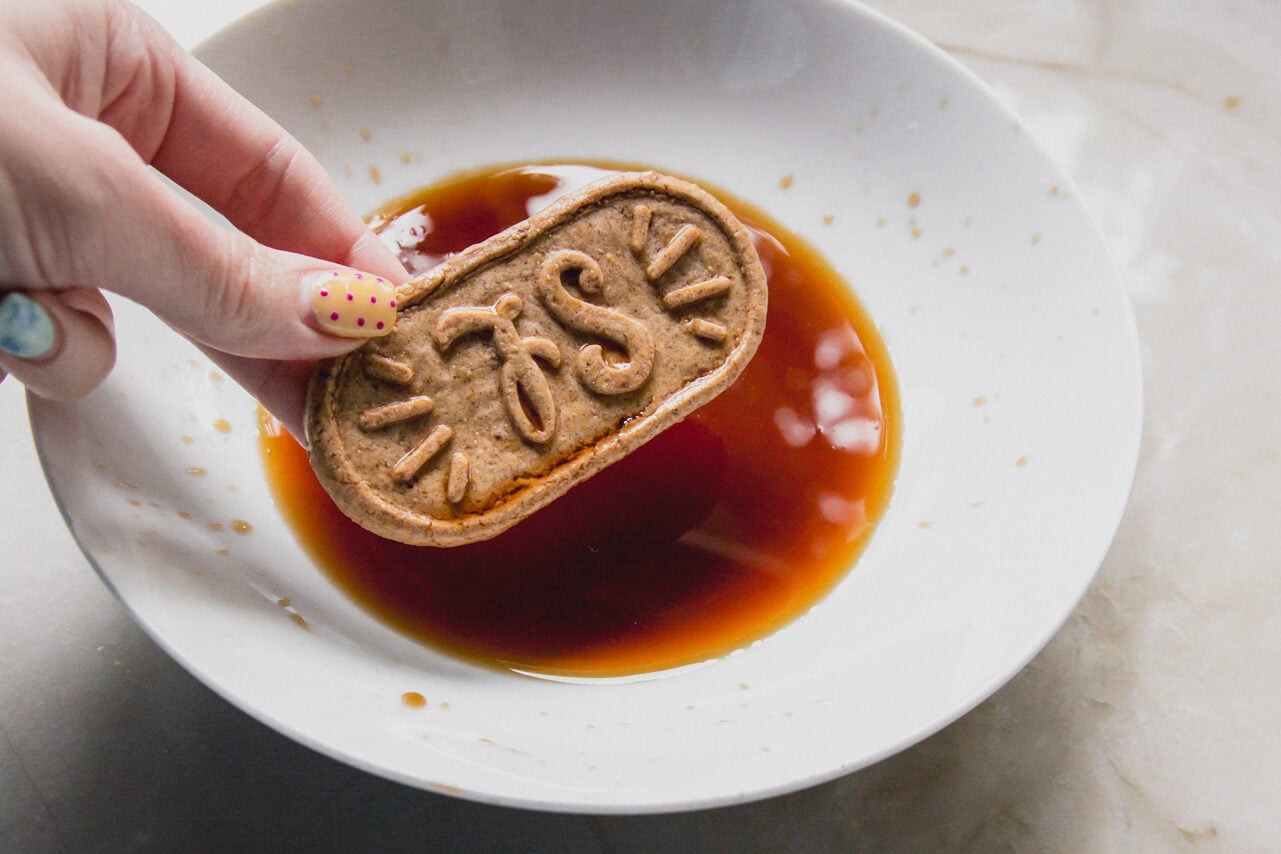 A breakfast biscuit being dipped into coffee in a white bowl by a hand.