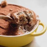 Protein tiramisu in a small yellow dish with a spoon scooping out a scoop.