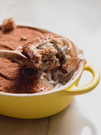 Protein tiramisu in a small yellow dish with a spoon scooping out a scoop.