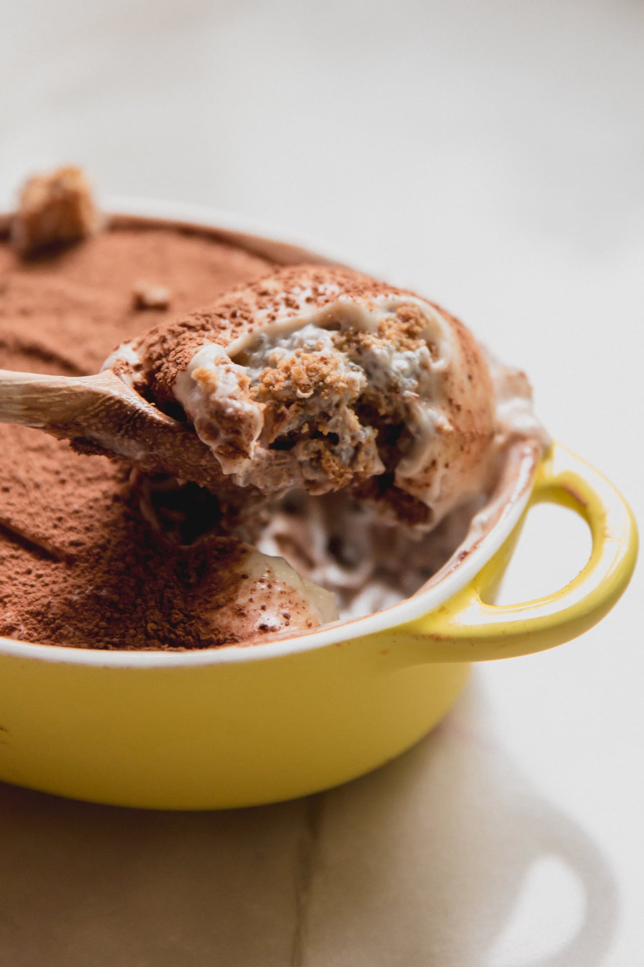 Protein tiramisu in a small yellow dish with a spoon scooping out a scoop.