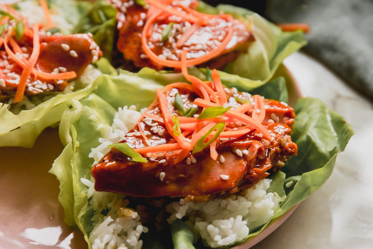 Teriyaki salmon lettuce cups topped with shredded carrots on a pink plate.
