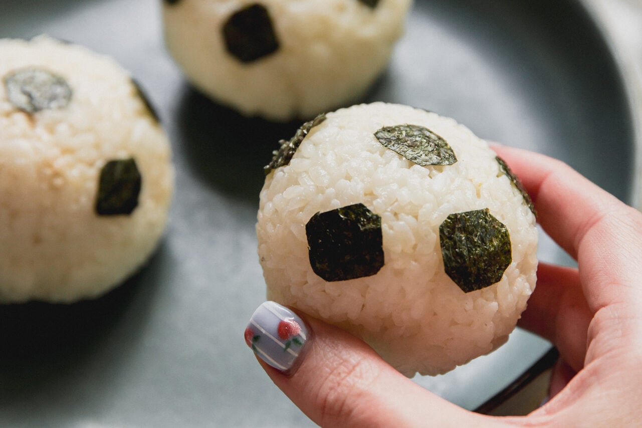 A plate with soccer tuna rice balls with a hand lifting one of the balls up.