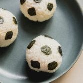 Three rice balls in a green bowl decorated with seaweed to resemble soccer balls.