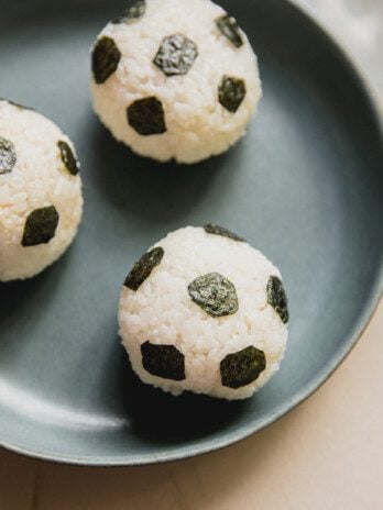 Three rice balls in a green bowl decorated with seaweed to resemble soccer balls.