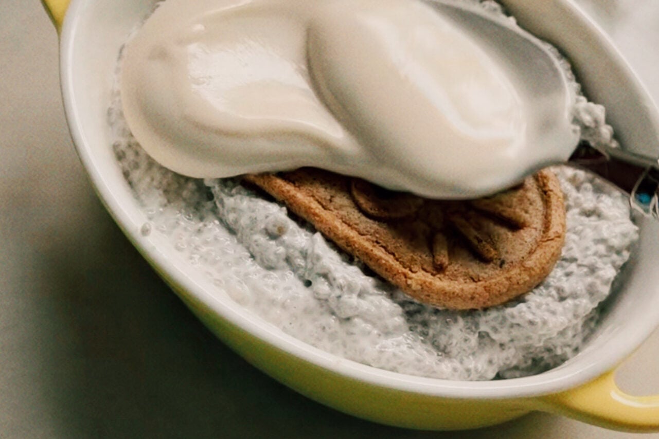 A ramekin filled with chia seed mixture with a breakfast biscuit on top and a spoon adding yogurt over the top.