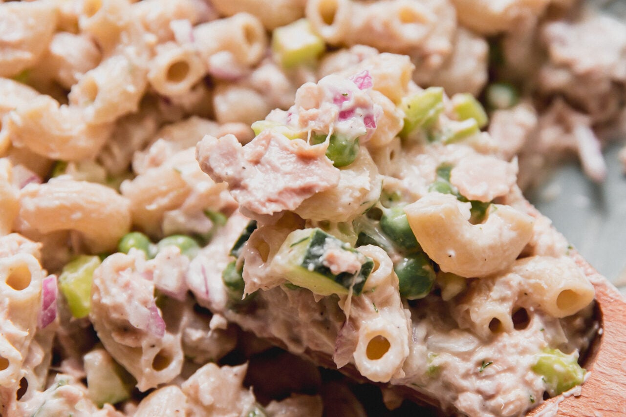 Tuna pasta salad in a bowl with a wooden spoon scooping a serving.