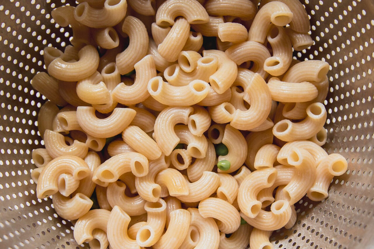 Cooked elbow pasta and peas in a pasta strainer.