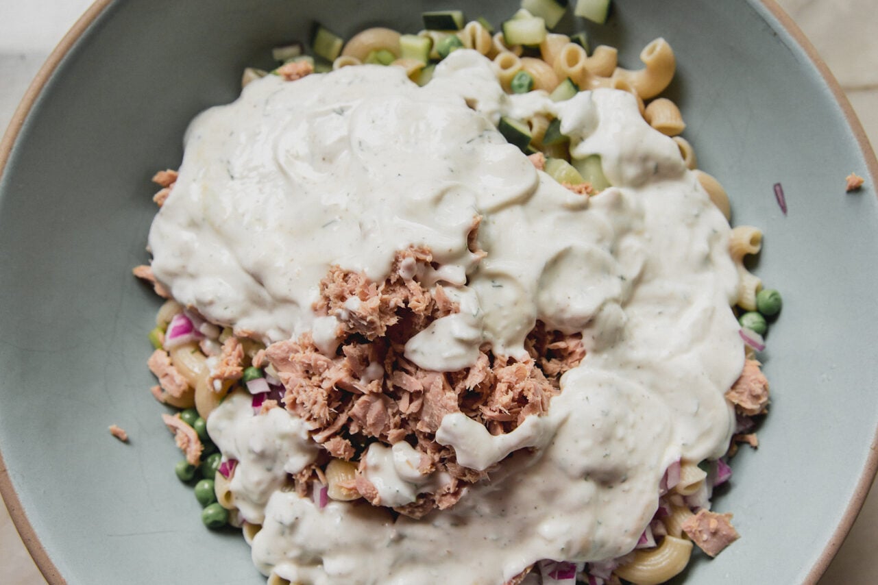 Tuna pasta salad in a large bowl topped with dressing, unmixed.