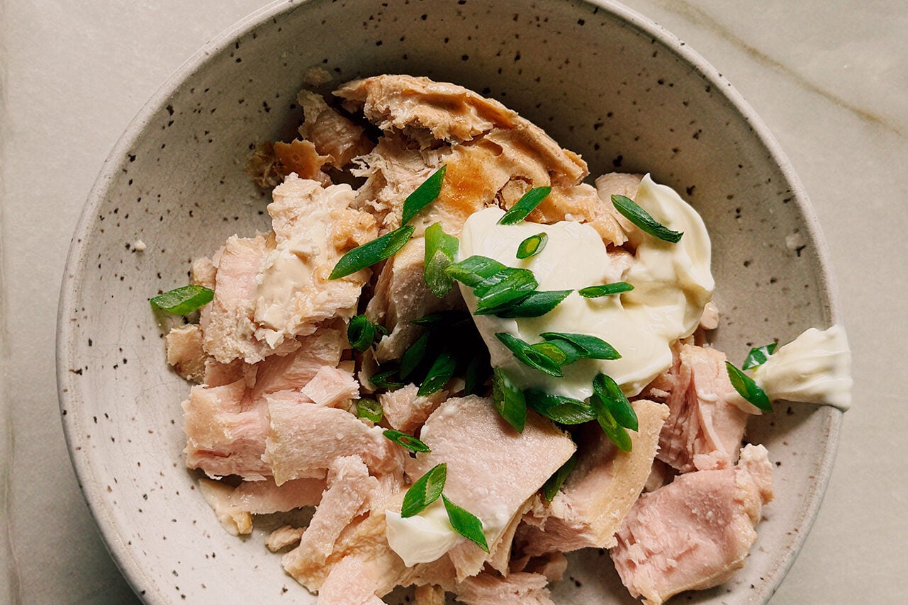 A white bowl filled with tuna, mayo, and green onions before being mixed together.