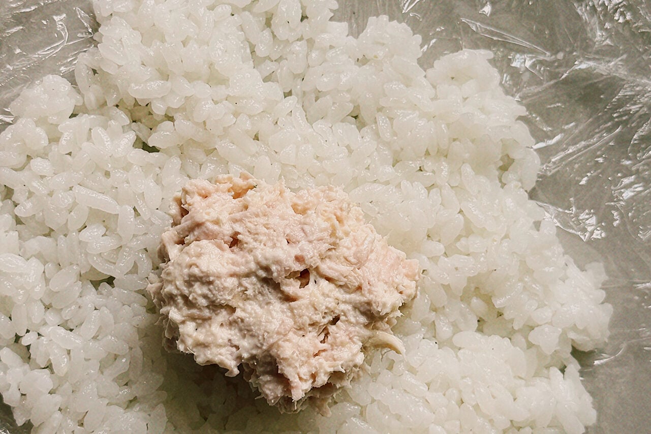 Cling wrap filed with a layer of rice and a scoop of tuna salad in the middle.