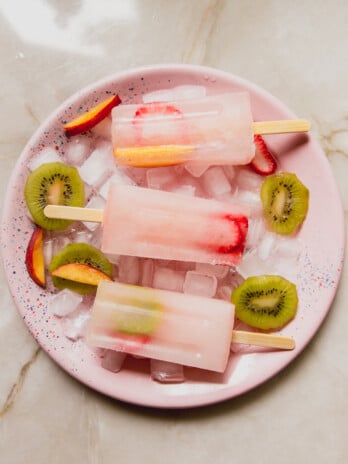 Three ginger and fruit popsicles on a pink plate.