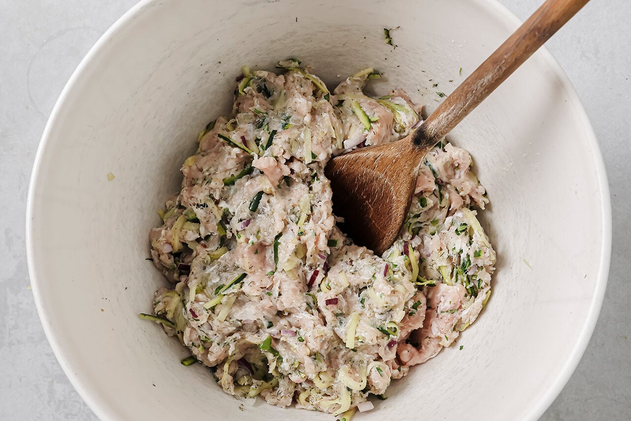 A white ceramic bowl filled with all the ingredients for Greek chicken burgers mixed together.