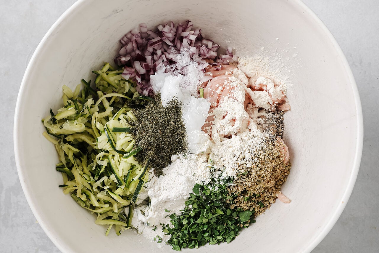 A white ceramic bowl filled with all the ingredients to make Greek chicken burgers.