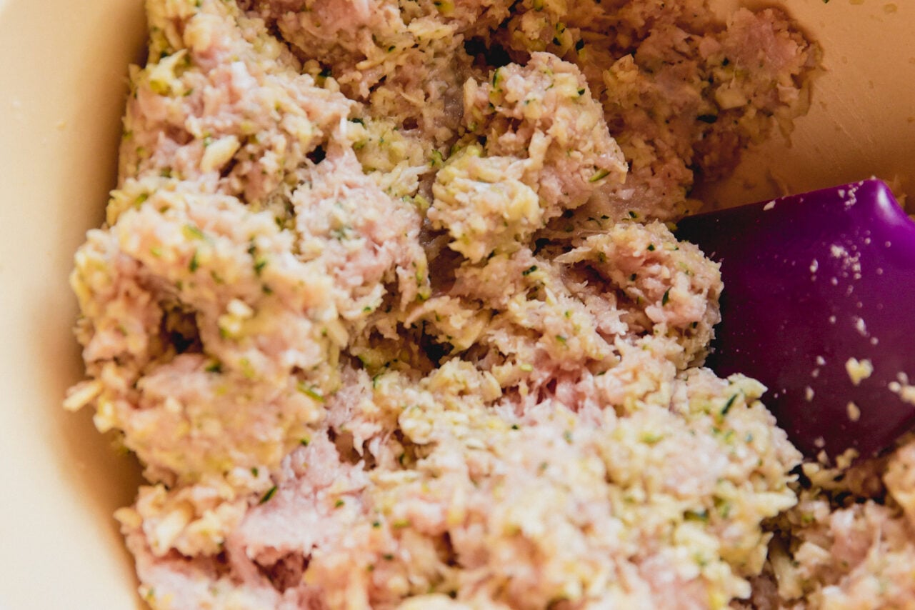 A white bowl filled with all the ingredients to make zucchini veggie chicken nuggets before mixing.