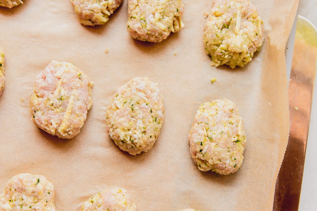 A baking sheet topped with parchment paper with zucchini veggie chicken nuggets on it before baking.