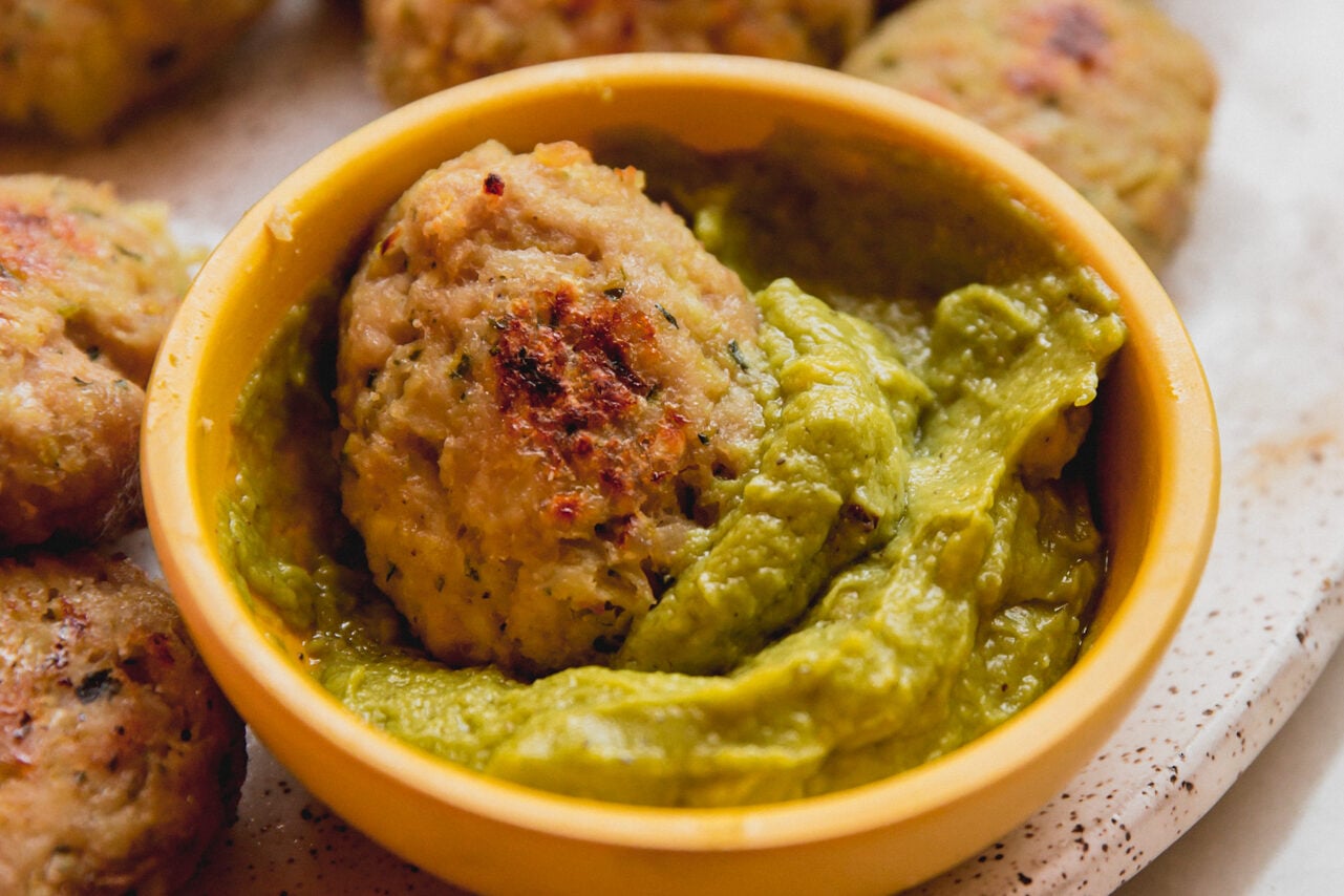 A speckled plate with a yellow bowl of guacamole with one nugget dipped in the guacamole.