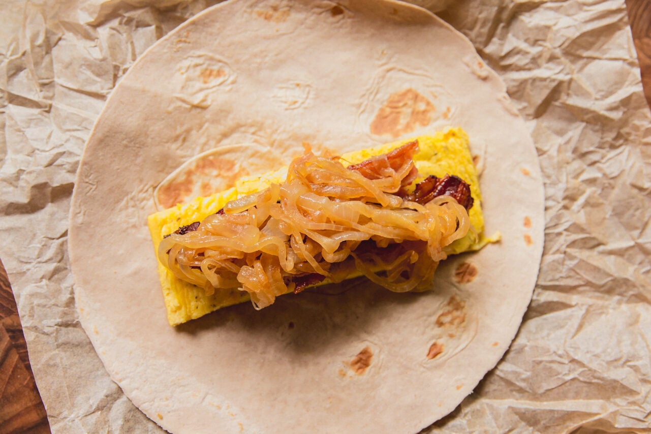 A caramelized onion breakfast burrito after being assembled with eggs, bacon, and onions before being rolled.