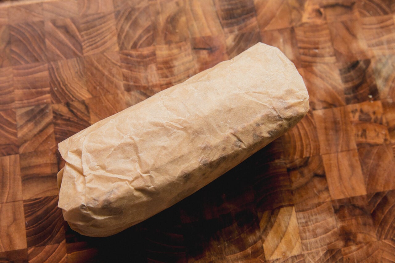 A caramelized onion breakfast burrito after being rolled with parchment paper. 