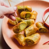 A plate of fried paper fried pickles sliced in half with one being held up by a tooth pick.